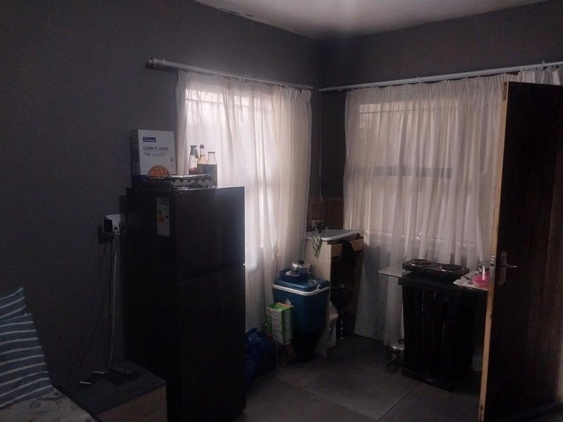A small kitchen area featuring tiled flooring and window treatments, currently utilized with basic appliances and storage.