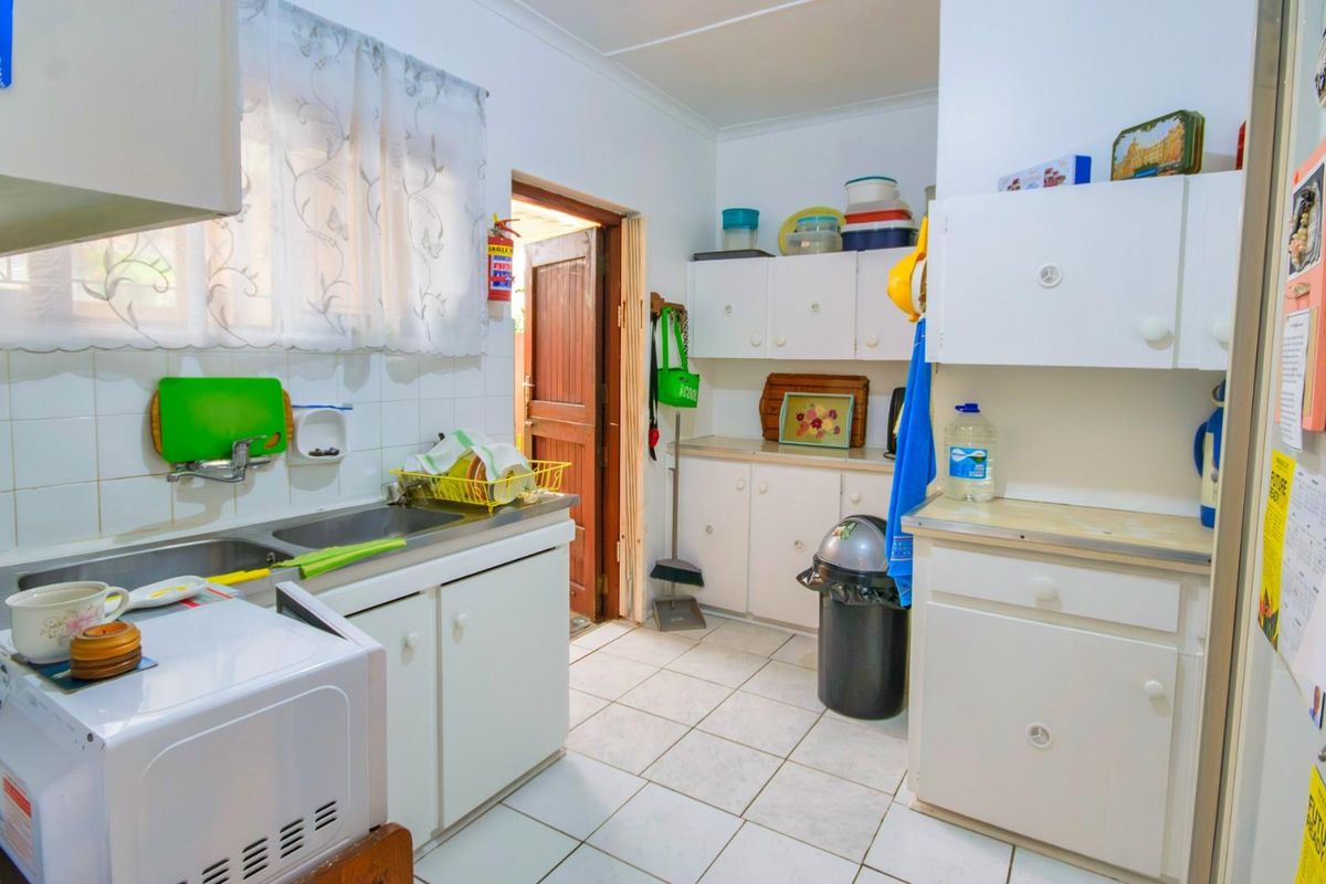 A functional kitchen featuring white cabinetry, tiled splashbacks, a stainless steel sink, and direct access to the exterior.