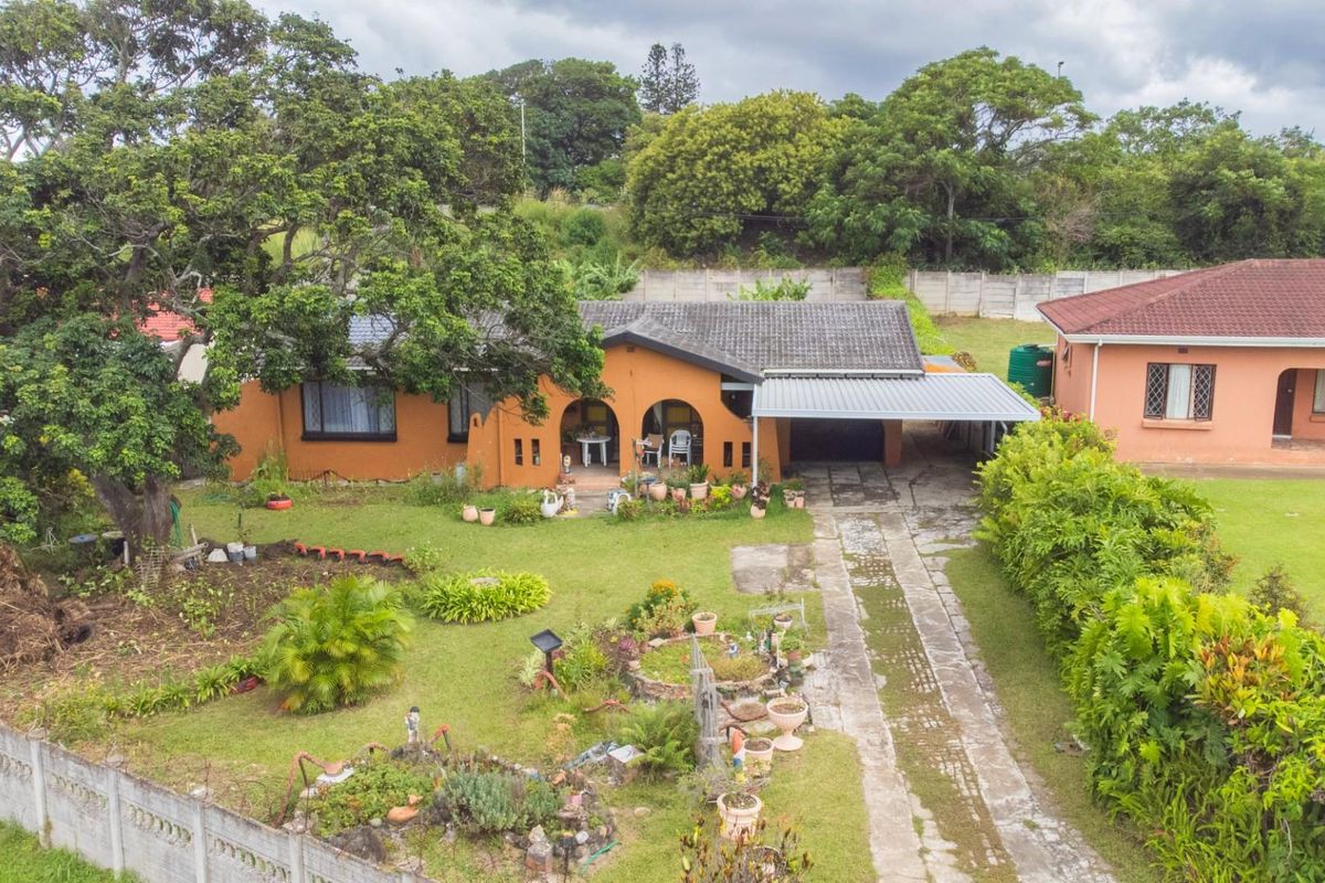 Aerial view of a residential property featuring a tiled roof, covered carport, and a spacious garden with established trees and perimeter walling.