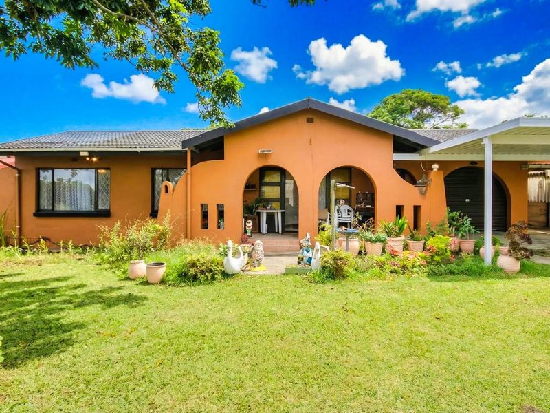Single-story residential home featuring a covered front porch with arched architectural details, a paved carport, and a well-established front garden.