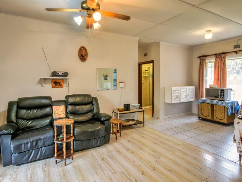 Open plan living area featuring wood-look laminate flooring, ceiling fan, and tiled transition area leading to a secondary space.