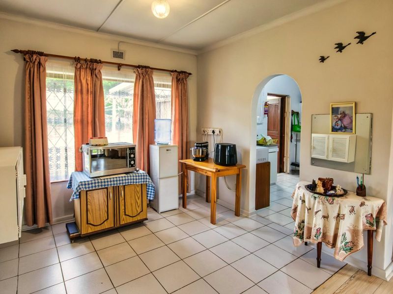 A functional living area featuring ceramic floor tiles, an arched doorway leading to an adjacent space, and large windows with curtain fixtures.