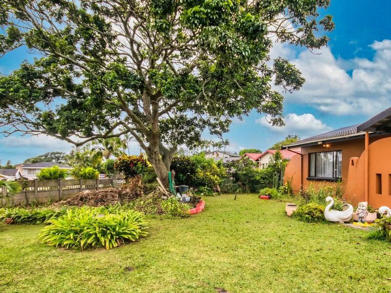 A spacious rear garden featuring a large mature tree, established landscaping, and a view of the rear building elevation.