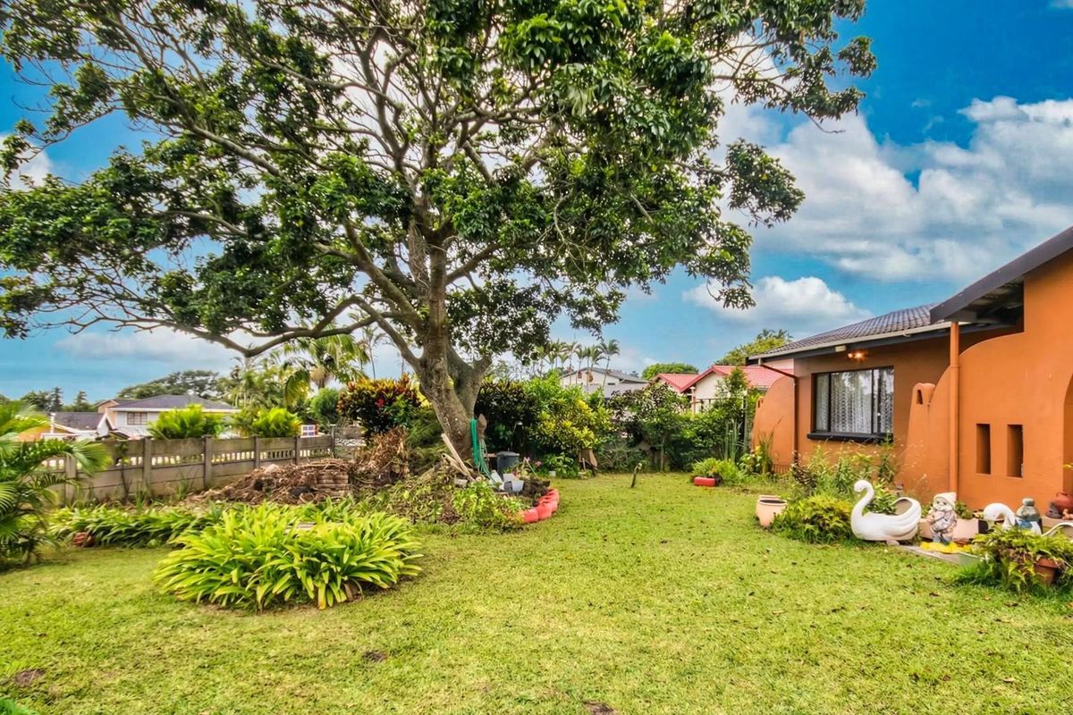 A spacious rear garden featuring a large mature tree, established landscaping, and a view of the rear building elevation.