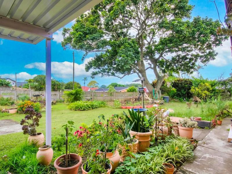 A covered patio overlooking a spacious rear garden featuring a large mature tree, established lawn, and perimeter boundary wall.