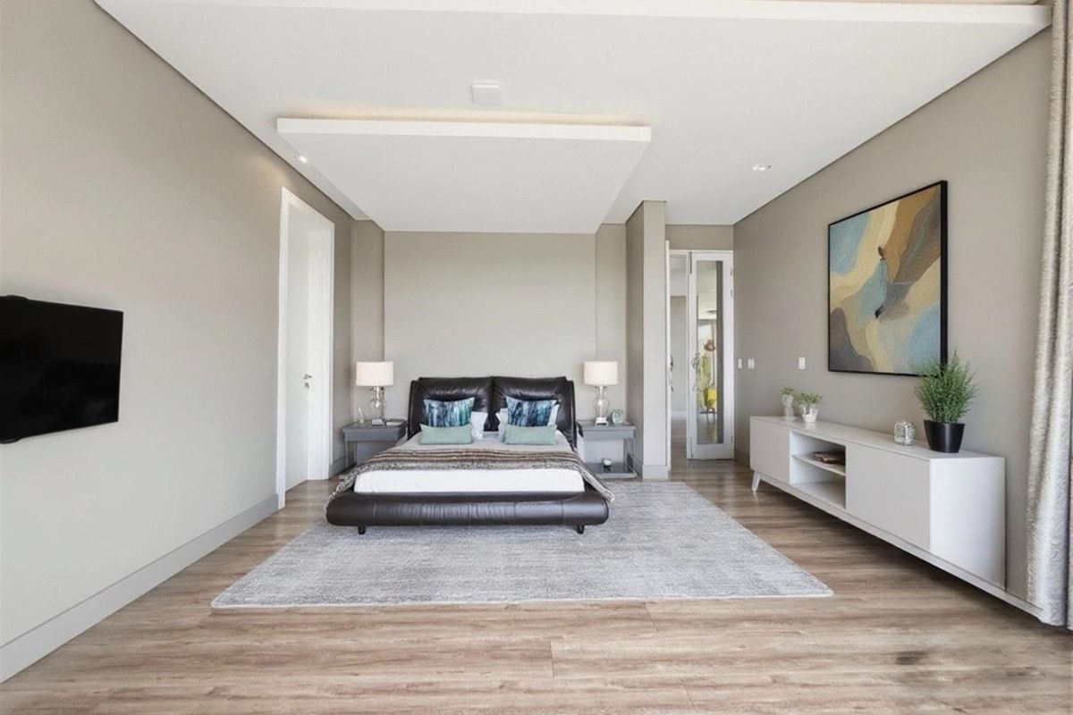 A spacious, modern bedroom featuring recessed ceiling lighting, wood-look flooring, and a neutral color palette, offering a clean and contemporary living space.