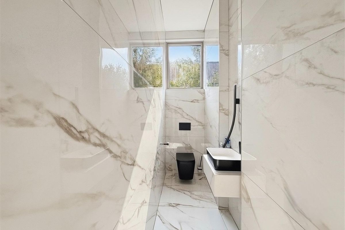 Modern bathroom featuring floor-to-ceiling marble-look tiling, a wall-mounted vanity with a contemporary basin, and a sleek wall-hung toilet.