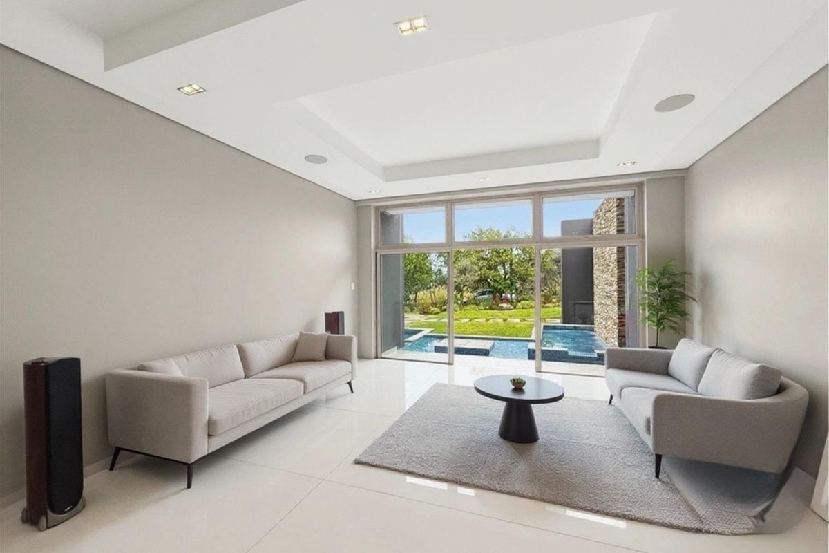 Spacious living room featuring high tray ceilings, large floor-to-ceiling windows, and direct views of the outdoor pool and garden area.