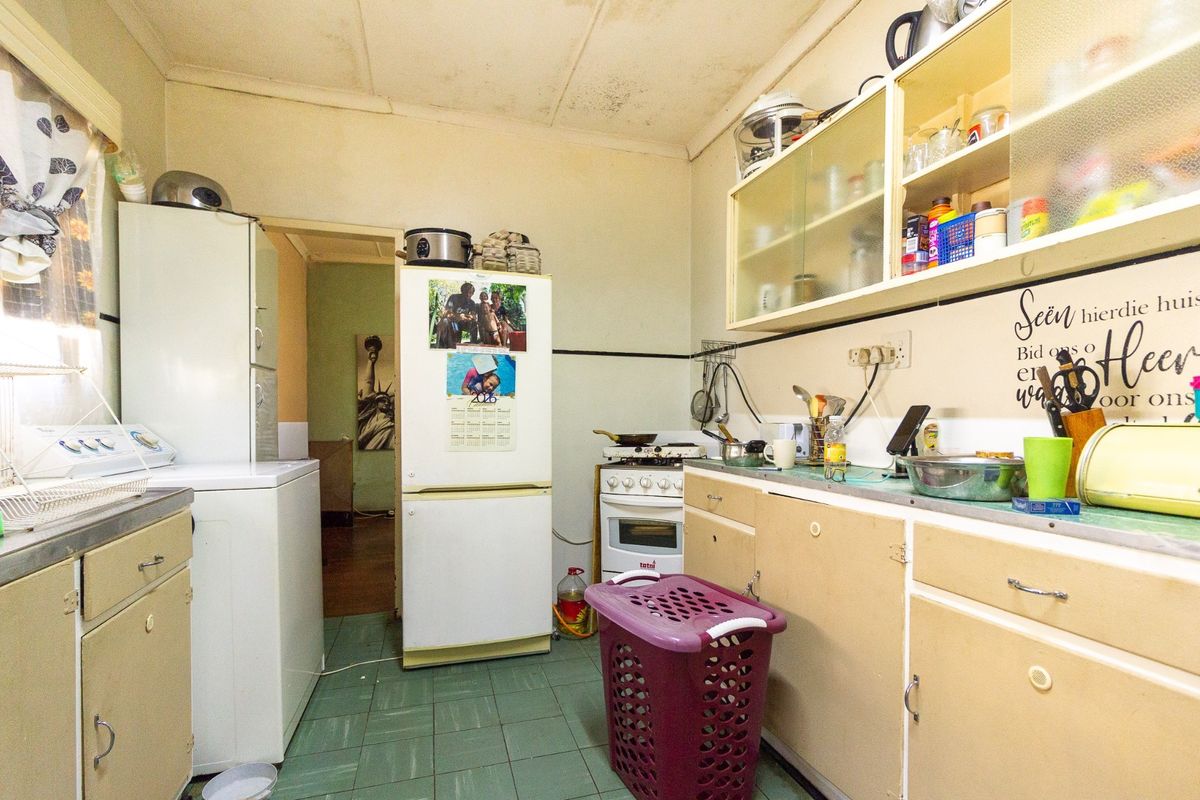 A functional kitchen space featuring built-in cabinetry, a freestanding stove, and tiled flooring, currently requiring cosmetic updates and ceiling repairs.