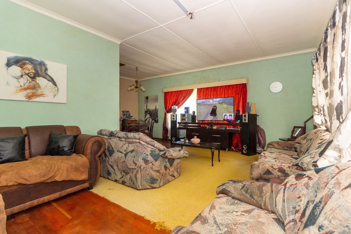 A spacious living room featuring a combination of hardwood and carpeted flooring with dated wall finishes and traditional ceiling tiles.
