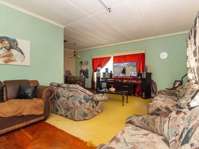 A spacious living room featuring a combination of hardwood and carpeted flooring with dated wall finishes and traditional ceiling tiles.