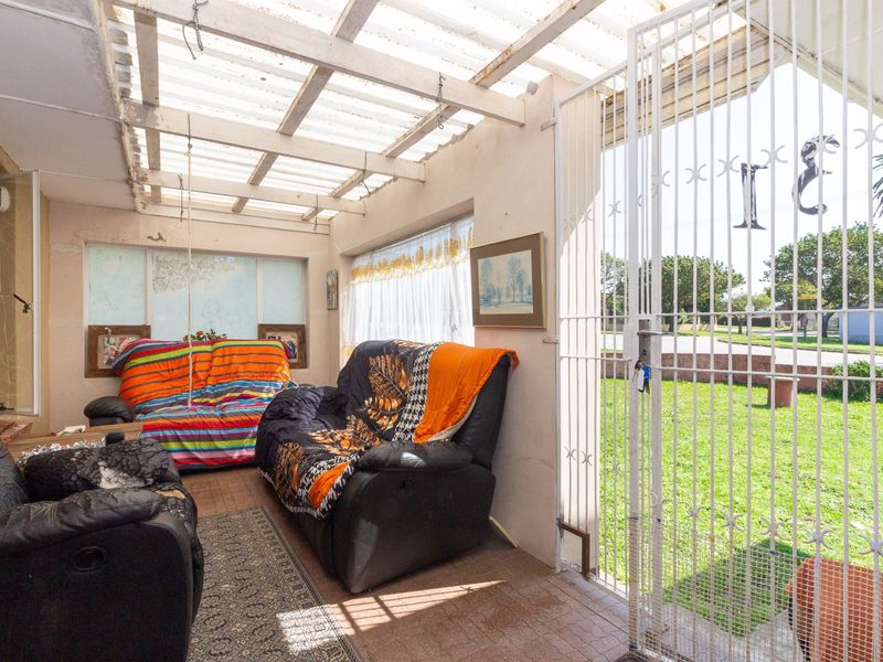 A covered patio area featuring a corrugated plastic roof, timber beams, and a security gate, providing direct access to the front garden.