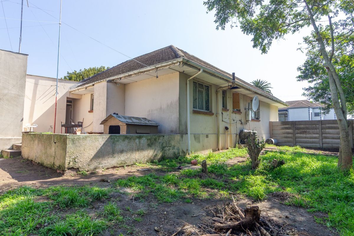 Rear view of the property showing the exterior facade, concrete retaining wall, and garden area requiring maintenance and landscaping.