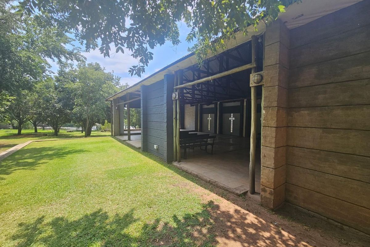 A view of the lodge exterior featuring a covered patio area with exposed timber beams and brick masonry walls overlooking a spacious garden.