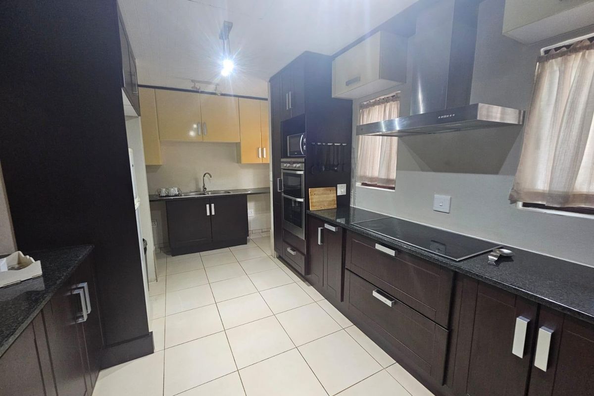 Modern kitchen featuring dark cabinetry, granite countertops, built-in oven, extractor fan, and tiled flooring.