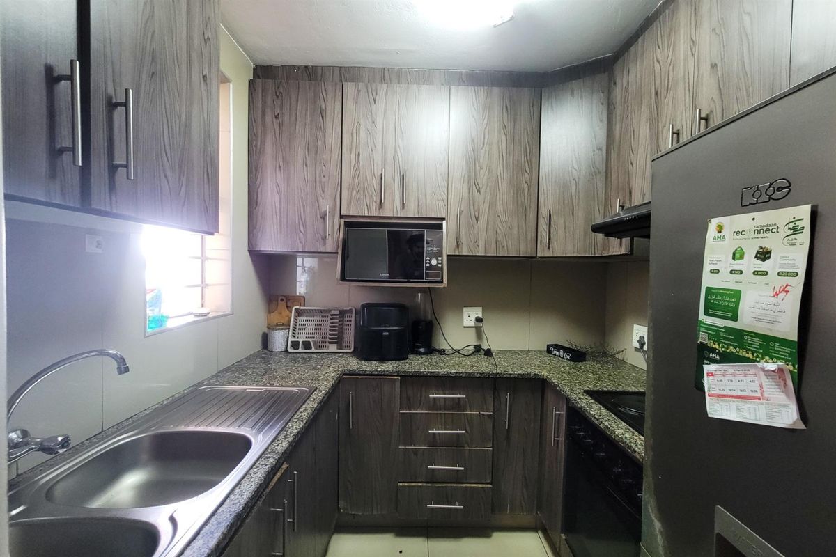 Compact kitchen featuring wood-look laminate cabinetry, granite countertops, a stainless steel double sink, and built-in appliances including a microwave and extractor fan.