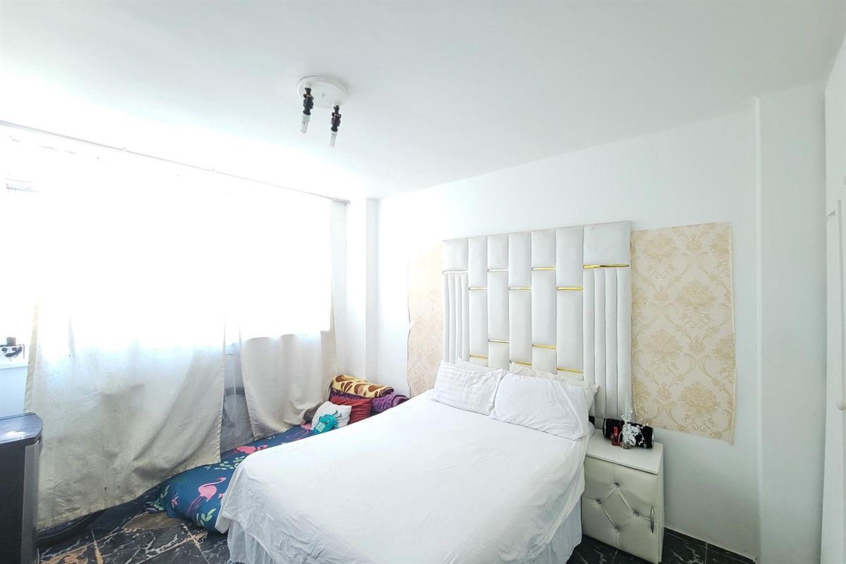 A bedroom featuring a large upholstered headboard, decorative wallpaper accents, and dark tiled flooring.