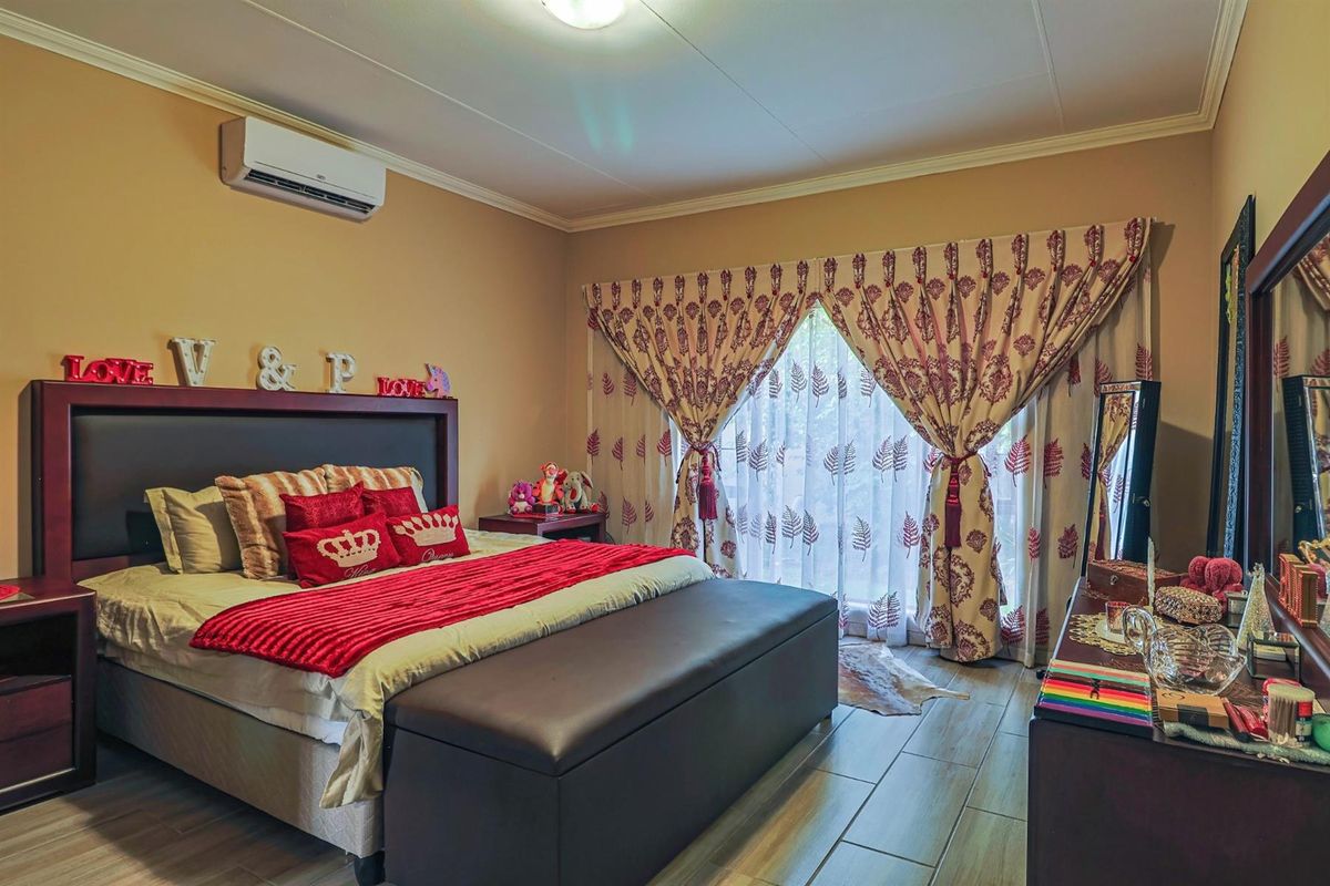 A well-maintained bedroom featuring tiled flooring, coving, and a wall-mounted split-system air conditioner, with large windows dressed in decorative curtains.