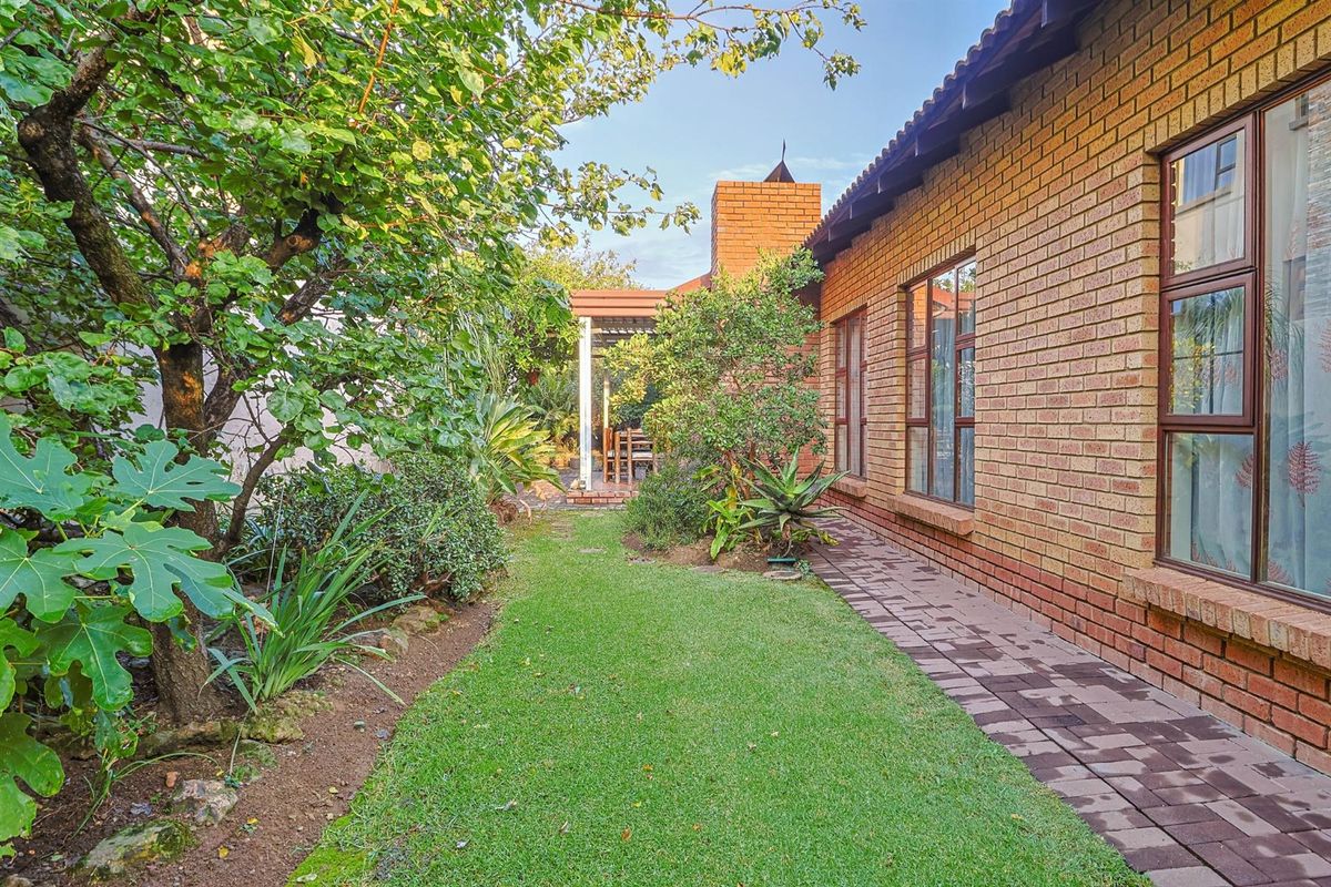 A well-maintained rear garden featuring a paved walkway, face brick exterior, and a covered patio area.