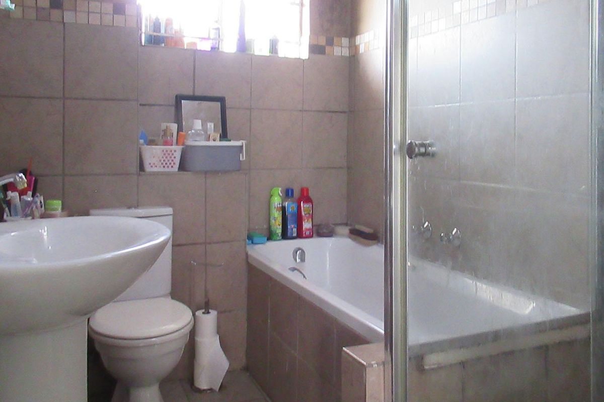 A functional bathroom featuring a pedestal basin, a standard toilet, and a combined bathtub and shower enclosure with tiled walls.