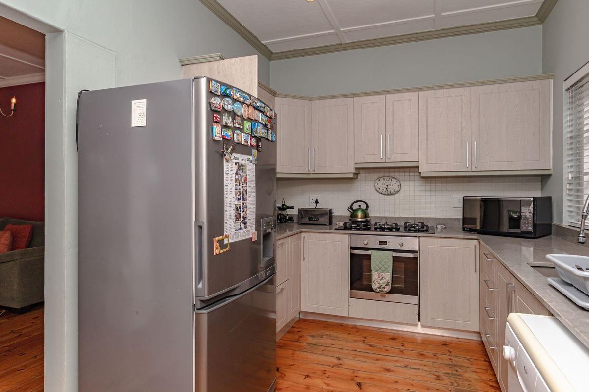 Functional kitchen featuring light-toned cabinetry, built-in oven, gas hob, and timber flooring, with an adjacent view into the living area.