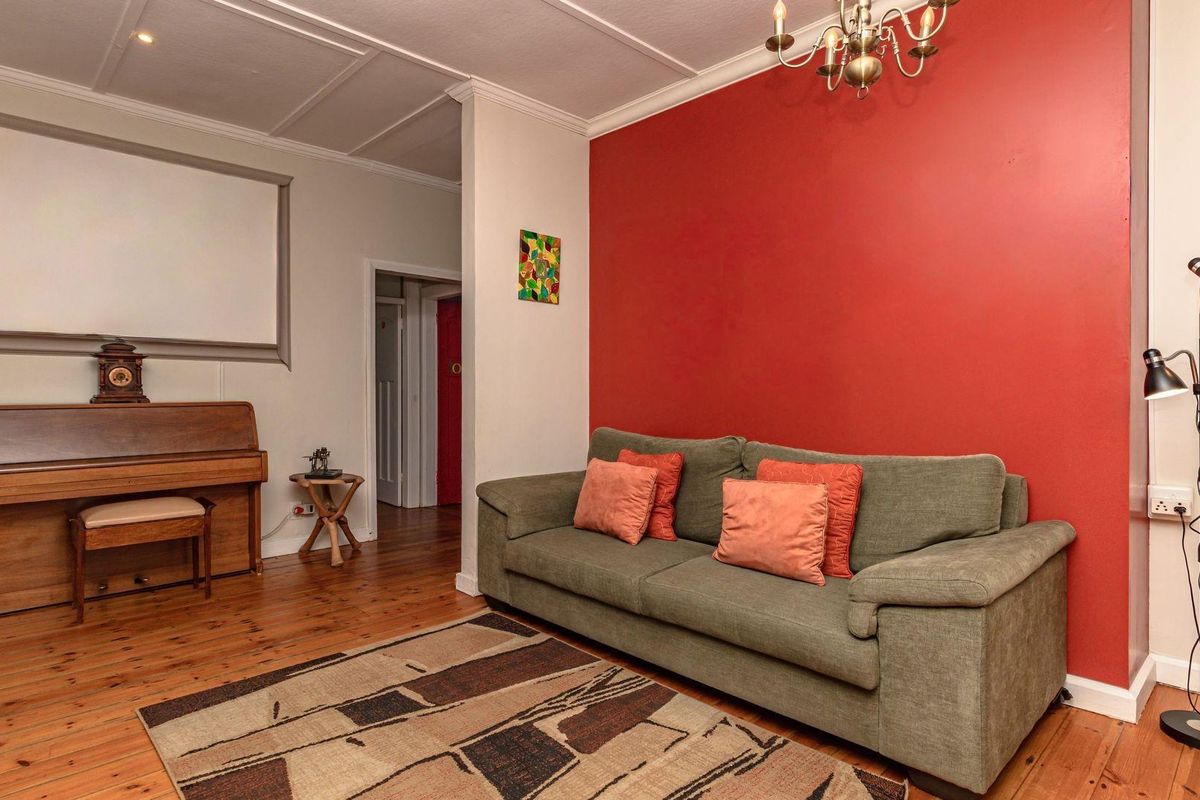 A living room featuring polished timber flooring, a bold red accent wall, and classic ceiling detailing.