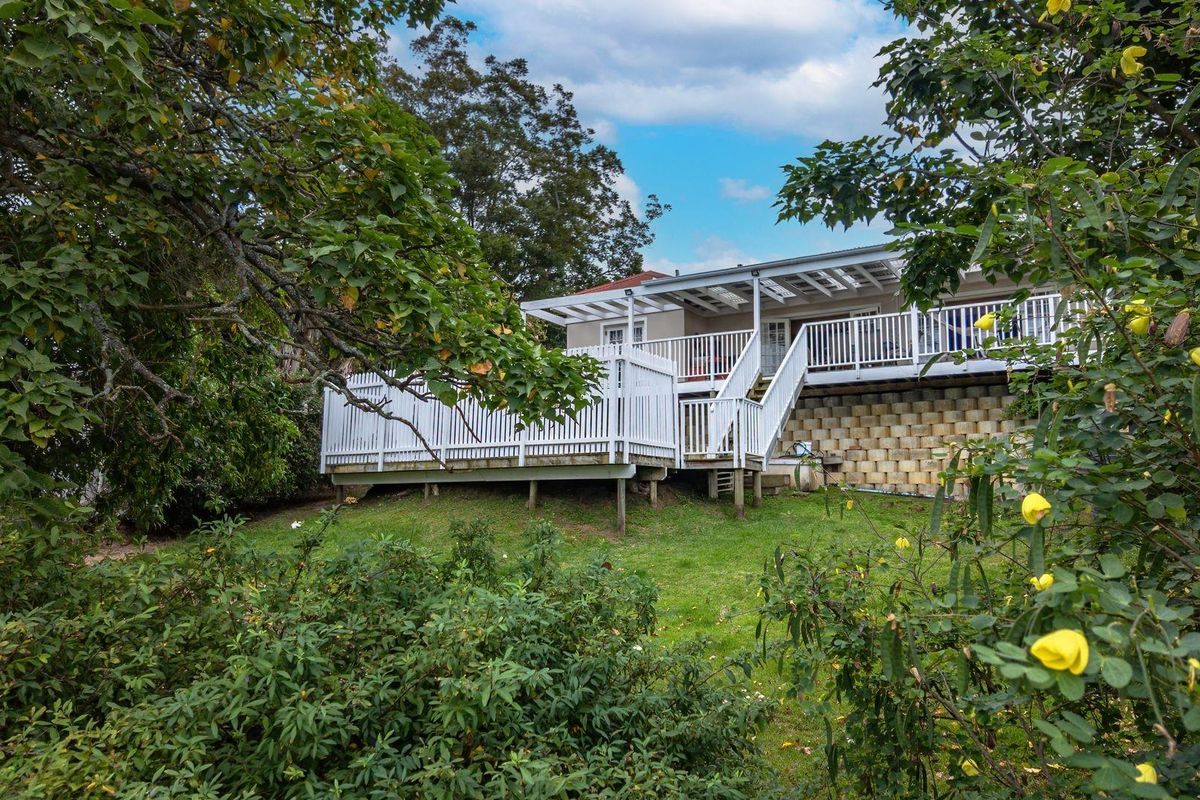 A rear view of the house featuring an elevated timber deck with white railings, a pergola, and a retaining wall overlooking the garden.