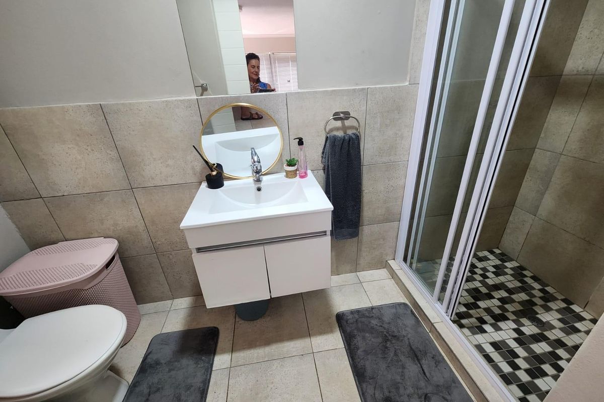 A functional bathroom featuring a modern wall-mounted vanity, a glass-enclosed shower with tiled flooring, and neutral wall tiling.