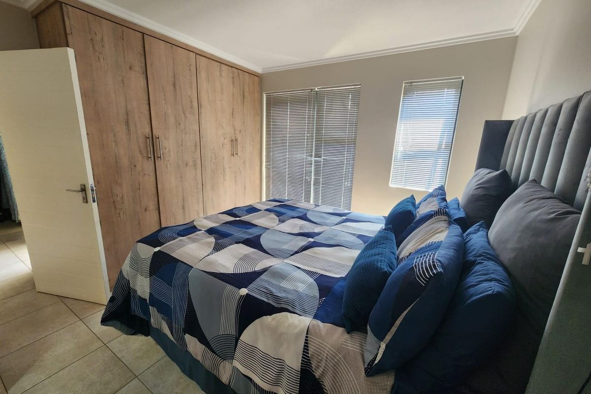 A well-maintained bedroom featuring built-in wooden wardrobes, tiled flooring, and venetian blinds on the windows.