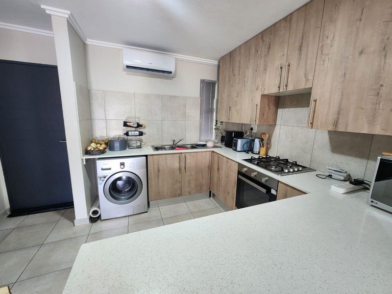 A functional kitchen featuring wood-look cabinetry, stone-style countertops, a built-in oven with gas hob, and an integrated laundry connection.