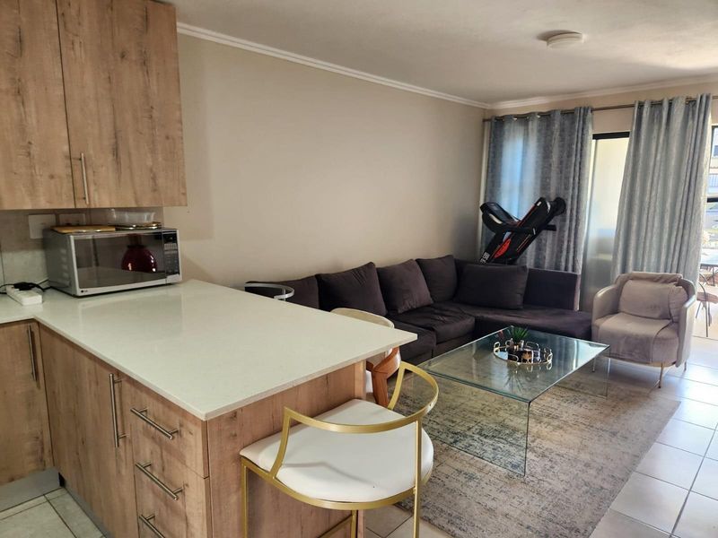 Open-plan living area featuring a modern kitchen with wood-look cabinetry, stone countertops, and a breakfast bar flowing into the lounge space.