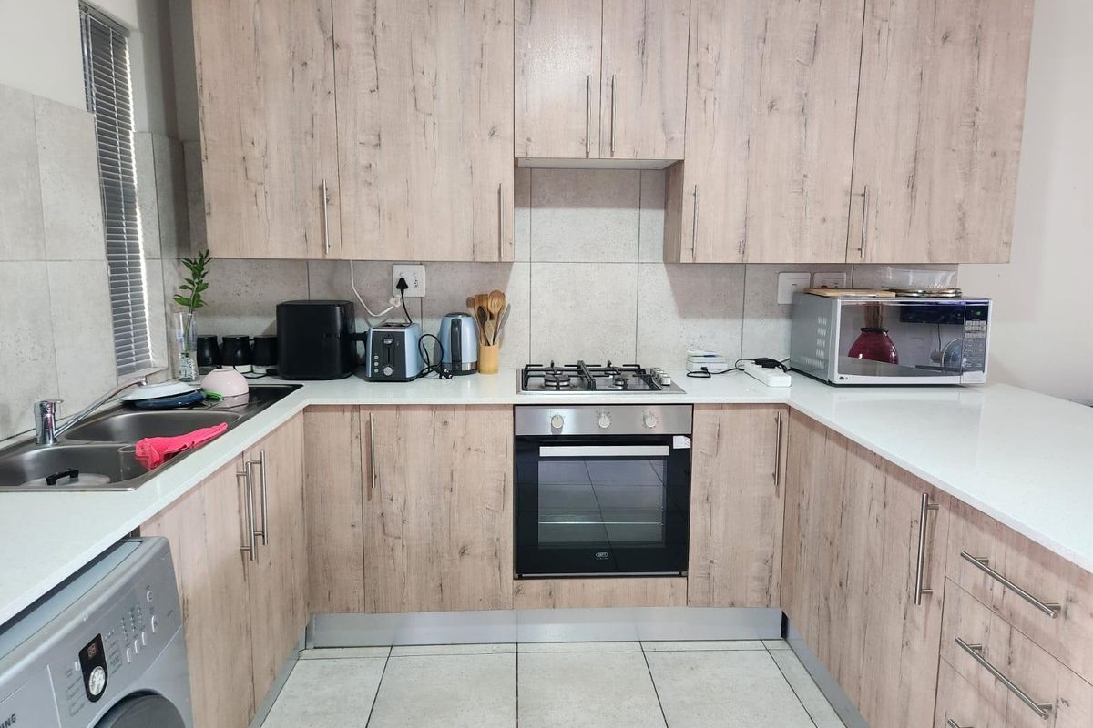 A functional U-shaped kitchen featuring light wood-grain cabinetry, stone-look countertops, a built-in gas hob, oven, and integrated space for a washing machine.