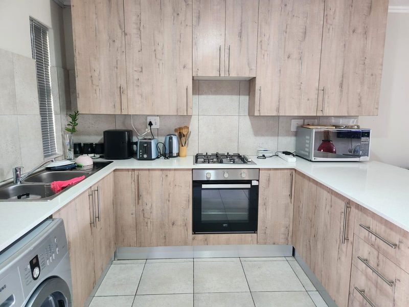 A functional U-shaped kitchen featuring light wood-grain cabinetry, stone-look countertops, a built-in gas hob, oven, and integrated space for a washing machine.