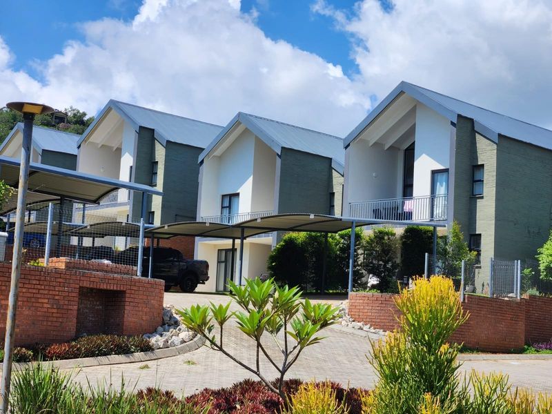 Exterior view of modern townhouse units featuring pitched roofs, brick and plaster facades, and covered carport parking areas.