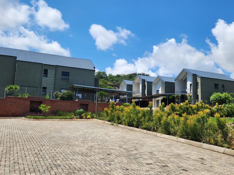 Exterior view of a modern townhouse complex featuring paved driveway, landscaped garden beds, and multi-story residential units with pitched metal roofing.
