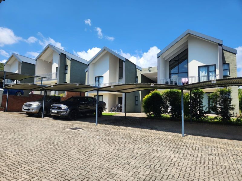 Exterior view of a modern townhouse complex featuring covered parking bays, paved driveway, and multi-level residential units with balconies.