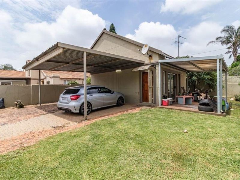 Rear view of the property featuring a paved driveway, a metal carport, a covered patio area, and a private garden space.