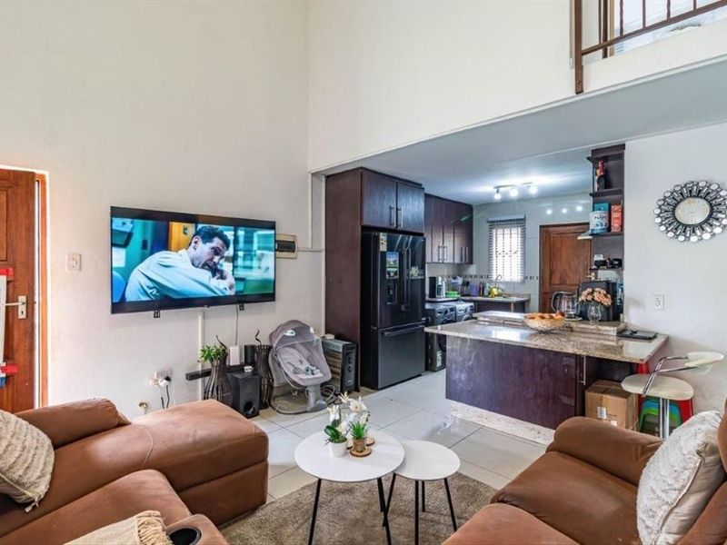 Open-plan living area featuring a kitchen with dark cabinetry, granite countertops, and a breakfast bar, flowing into a spacious lounge with high ceilings.