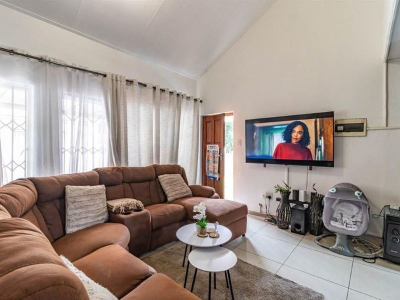 A bright living room featuring high vaulted ceilings, tiled flooring, and a wall-mounted television setup with direct access to the exterior.