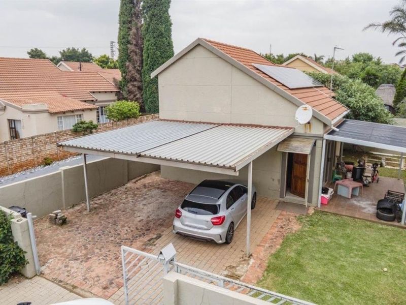 Aerial view of a residential property featuring a paved driveway, metal carport, solar panels, and a covered patio area.