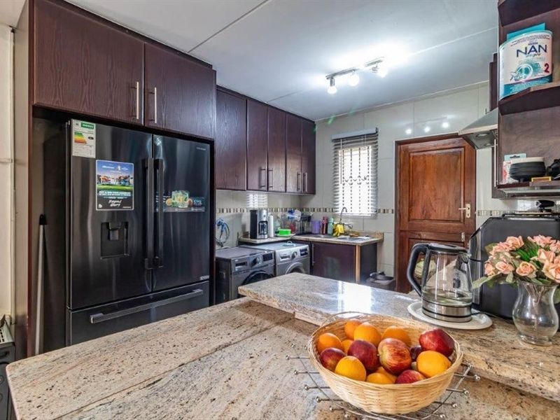 A functional kitchen featuring dark wood cabinetry, granite countertops, a breakfast bar, and integrated space for laundry appliances.