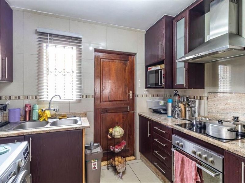 A functional kitchen featuring dark wood cabinetry, granite countertops, a stainless steel extractor fan, and a built-in oven with a ceramic hob.