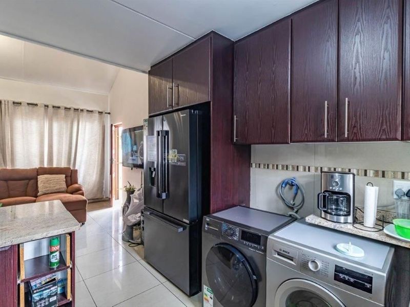 Open plan kitchen featuring dark wood cabinetry, granite countertops, and integrated laundry appliance connections, flowing into the adjacent living area.