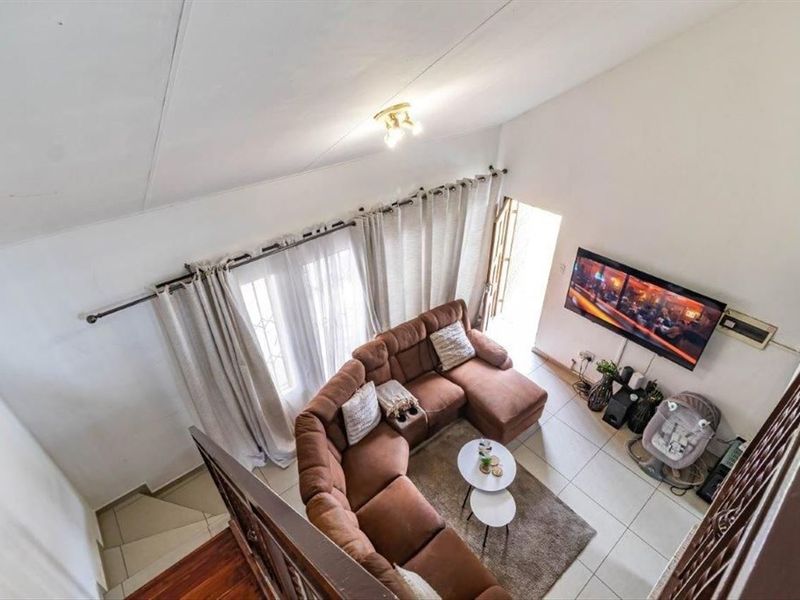 A high-angle view of a living room featuring tiled flooring, vaulted ceilings, and a wall-mounted television area with direct access to the exterior.
