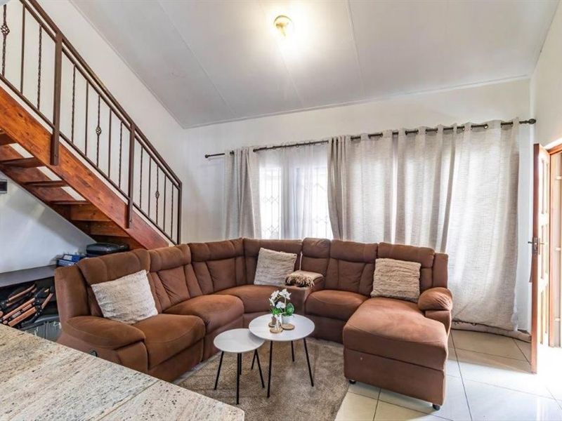 A living room featuring tiled flooring, a wooden staircase with metal railings, and large windows with curtains, providing access to the exterior.