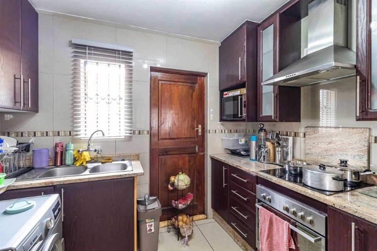 A functional kitchen featuring dark wood cabinetry, granite countertops, a stainless steel extractor fan, and a built-in oven with a ceramic hob.