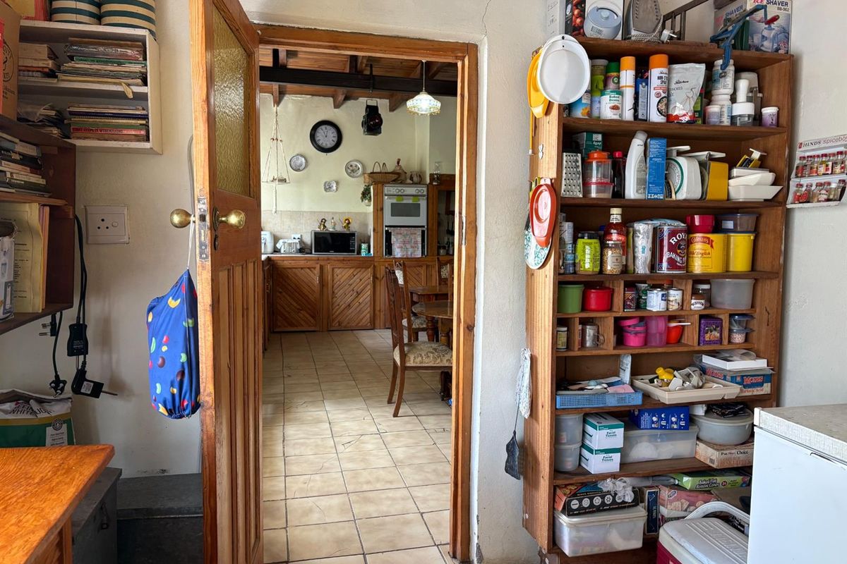 A view through a wooden doorway into a rustic kitchen area with tiled flooring and traditional timber cabinetry.