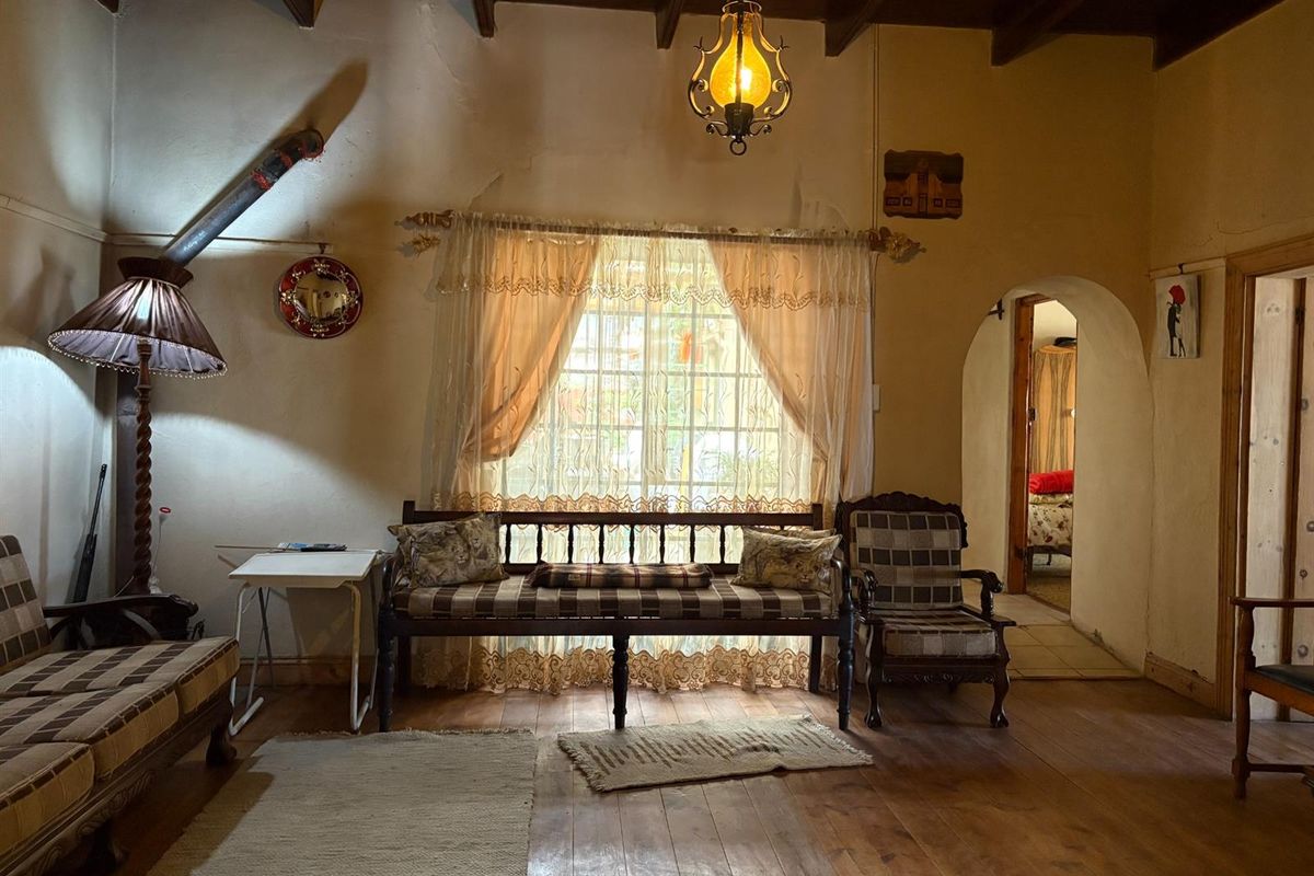 A rustic living room featuring exposed timber ceiling beams, hardwood flooring, and an arched doorway leading to an adjacent bedroom.