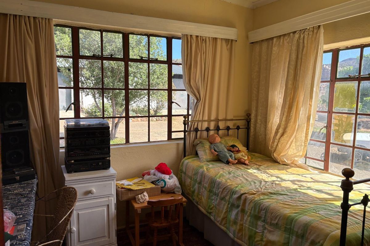 A bedroom featuring large steel-framed windows, neutral wall tones, and classic architectural proportions, offering a bright space with potential for modernization.