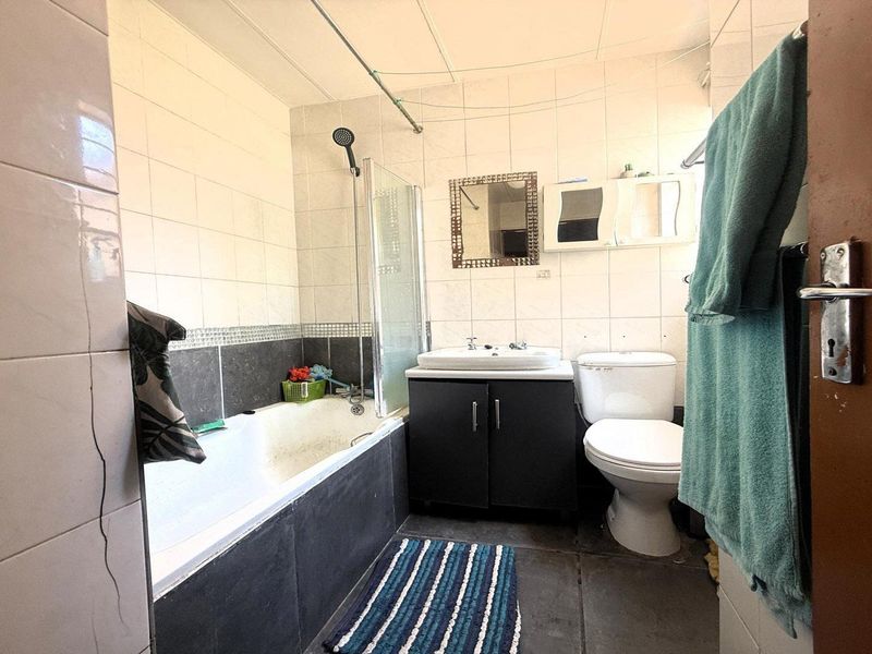 A functional bathroom featuring a bathtub with shower attachment, vanity basin, and toilet, finished with tiled walls and flooring.